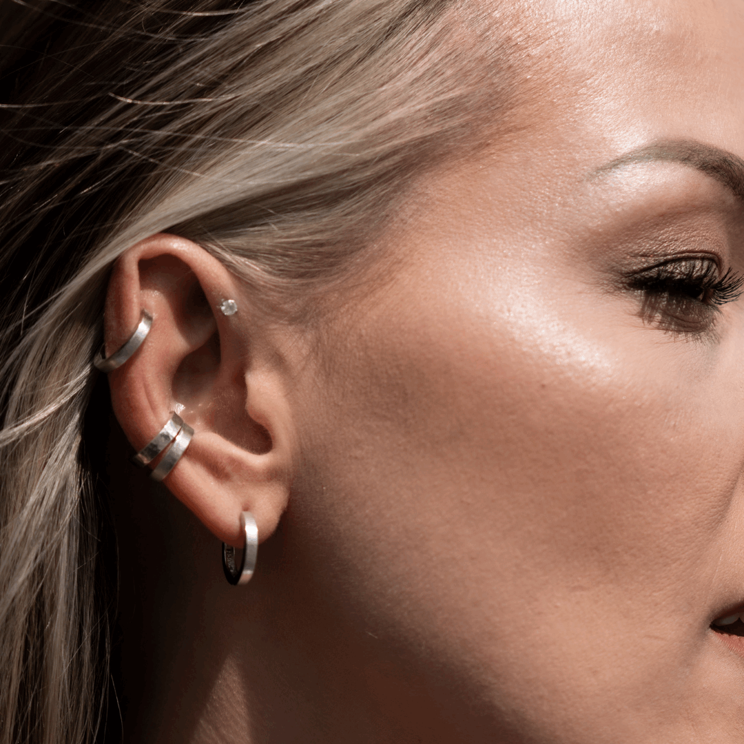 Close-up des Ohrs eines Modells mit dem Earcuff 'Anicca klein' aus recyceltem 925er Sterling Silber und weiterem Schmuck; handgefertigter Schmuck aus nachhaltigen Materialien in Deutschland.