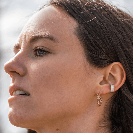 Moderner Earcuff 'Aura double' aus 14k Echtgold und Weißgold, getragen von einem braunhaarigen Modell im Seitenprofil zusammen mit einem anderen Ohrring; handgefertigter Schmuck aus nachhaltigen Materialien in Deutschland.